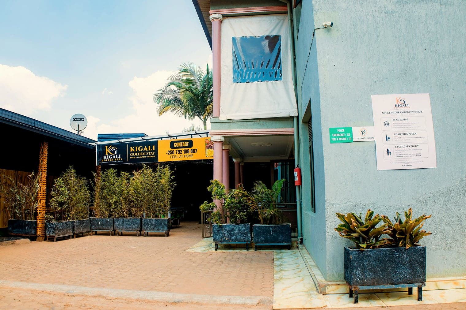 The paved courtyard with palms and planters, looking across to the Kigali Golden Stay sign
